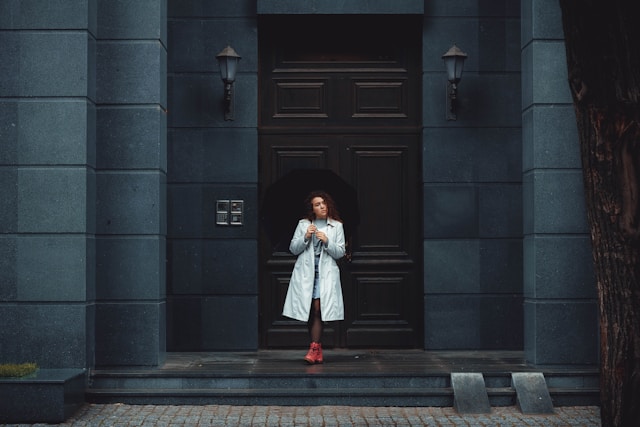 Woman in white coat standing at ornate building entrance representing opening the door to anxiety