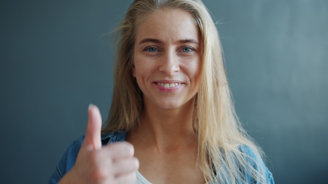 Woman with blonde hair giving thumbs up gesture showing confidence despite anxiety
