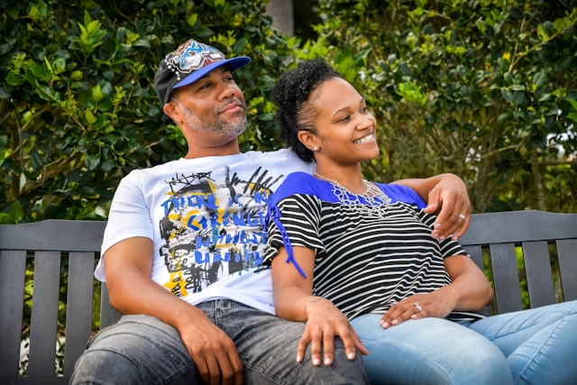 Smiling couple sitting outdoors on a park bench, leaning closely together.