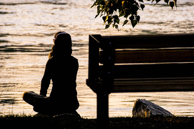 Silhouette of person meditating by water during sunset