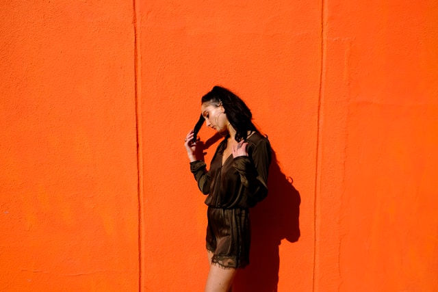 Woman leaning against a bright orange wall, smiling with confidence.