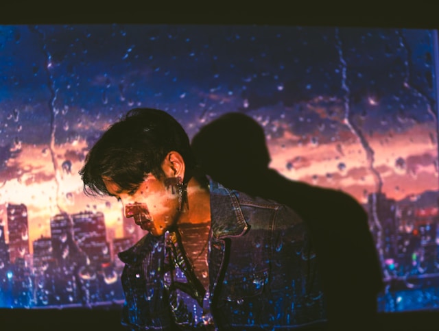 Person standing in shadow with rainy cityscape projected on a wall behind them.