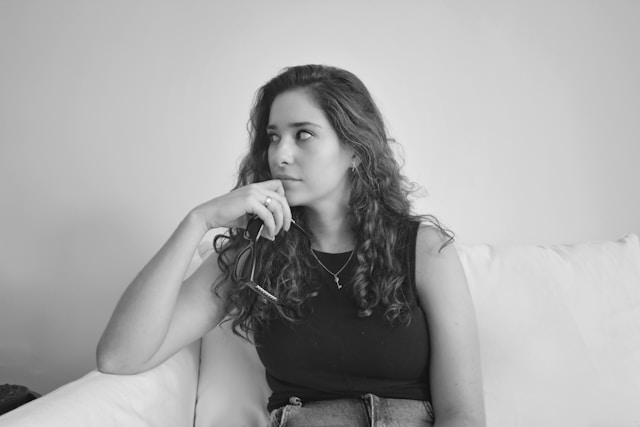 Young woman sitting on a couch, looking thoughtful and anxious.