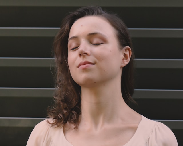 Young woman with eyes closed practicing diaphragmatic breathing exercise for anxiety relief