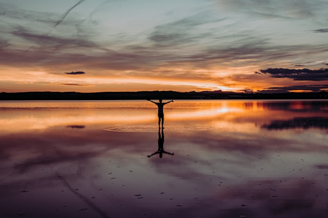 Person standing peacefully at sunset with arms outstretched symbolizing letting go of anxiety and embracing acceptance