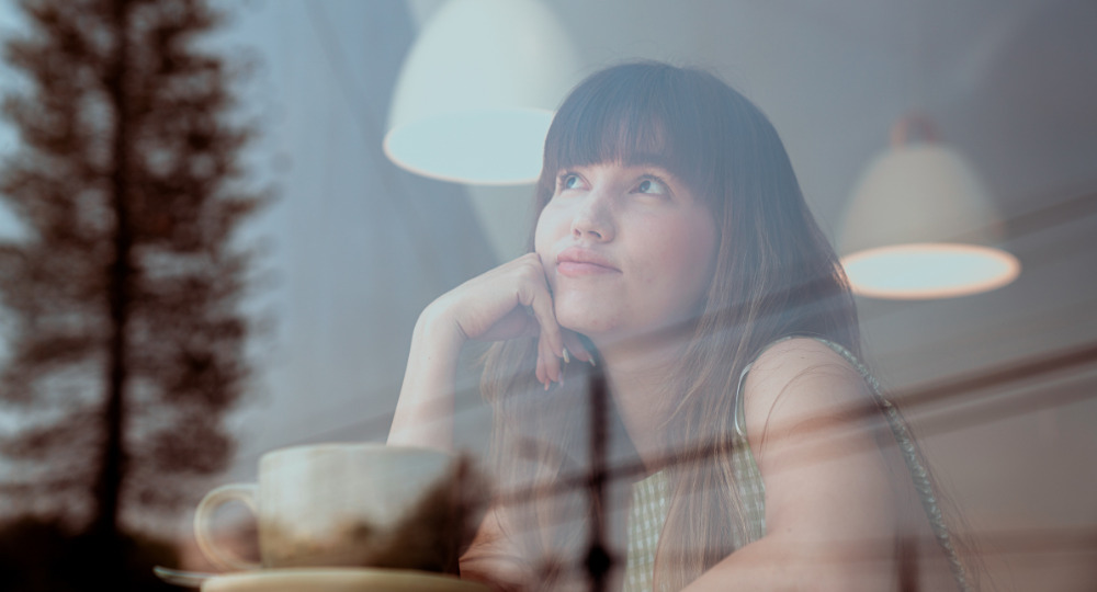 Woman in soft lighting looking upward thoughtfully with double exposure plant effect