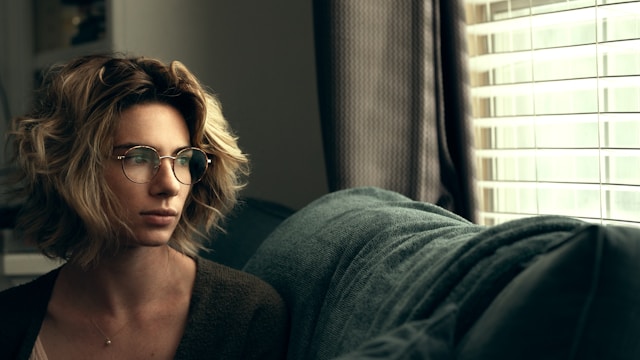Woman with glasses lying on couch looking anxious and contemplative