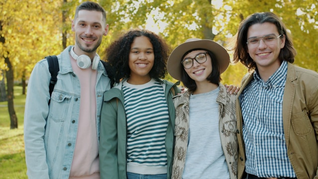 Four smiling friends standing together outdoors in a park.