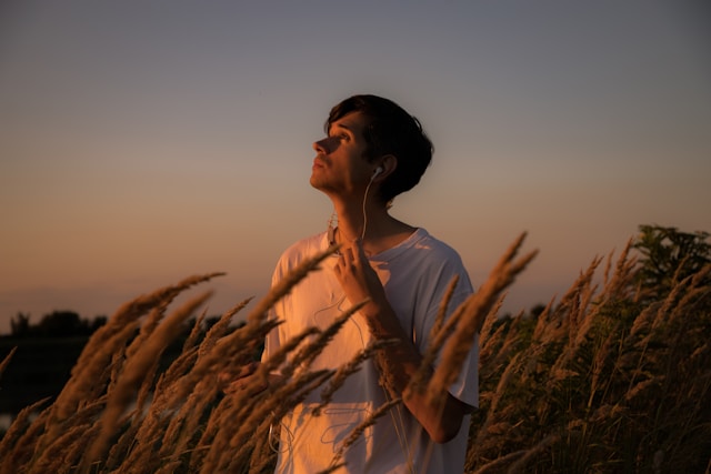 Person wearing headphones looking up at the sky while standing in a field at sunset