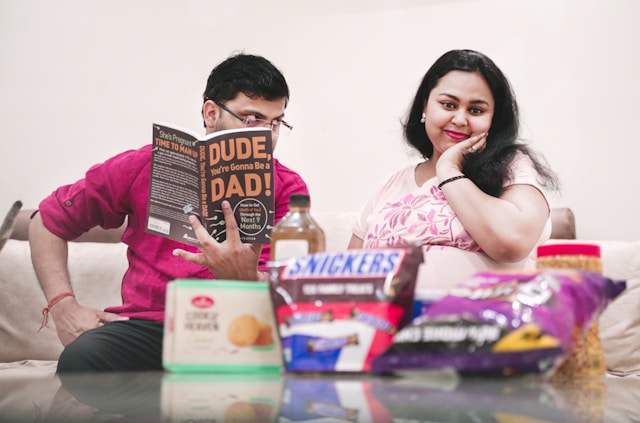 Expectant couple with parenting book and snacks, preparing for baby and preventing postpartum mental health issues