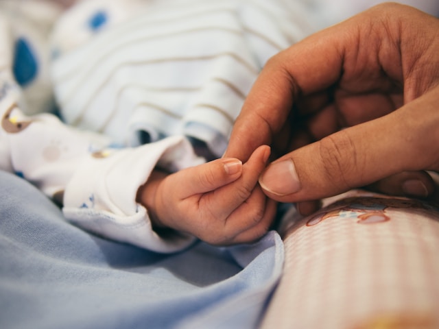 Close-up of parent's hand gently holding newborn baby's tiny hand, representing postpartum bonding