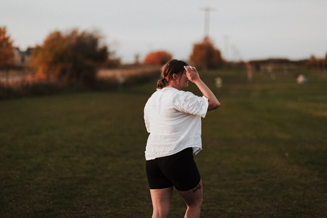 Woman walking outside in a field at sunset, wearing a white shirt and black shorts.