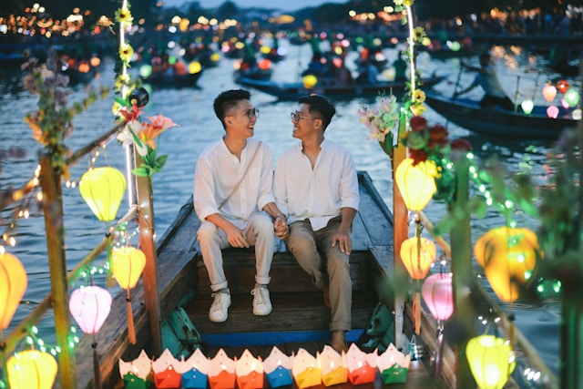 Two men in white clothing sitting together on decorated boat with colorful lanterns at night