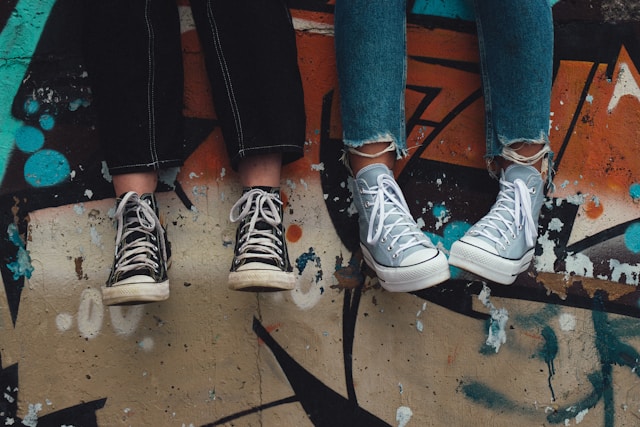 Close-up of two pairs of legs wearing jeans and canvas sneakers standing on colorful painted pavement