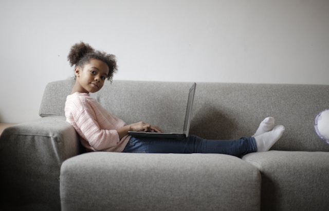 Young girl with natural hair sitting on gray couch using laptop computer